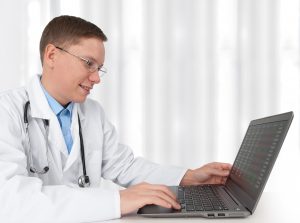 smiling male doctor working on computer; telehealth